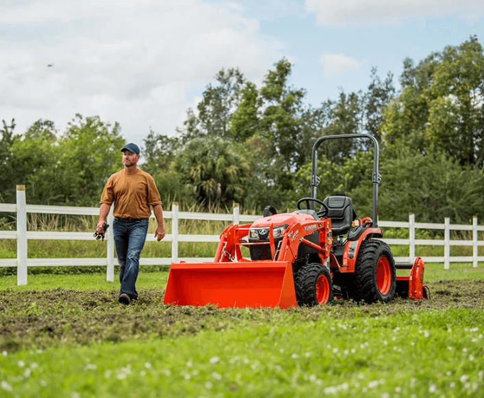 Kubota B2601 Utility Tractor with front loader and R14 hybrid tires being used on a grassy field for spring land maintenance.